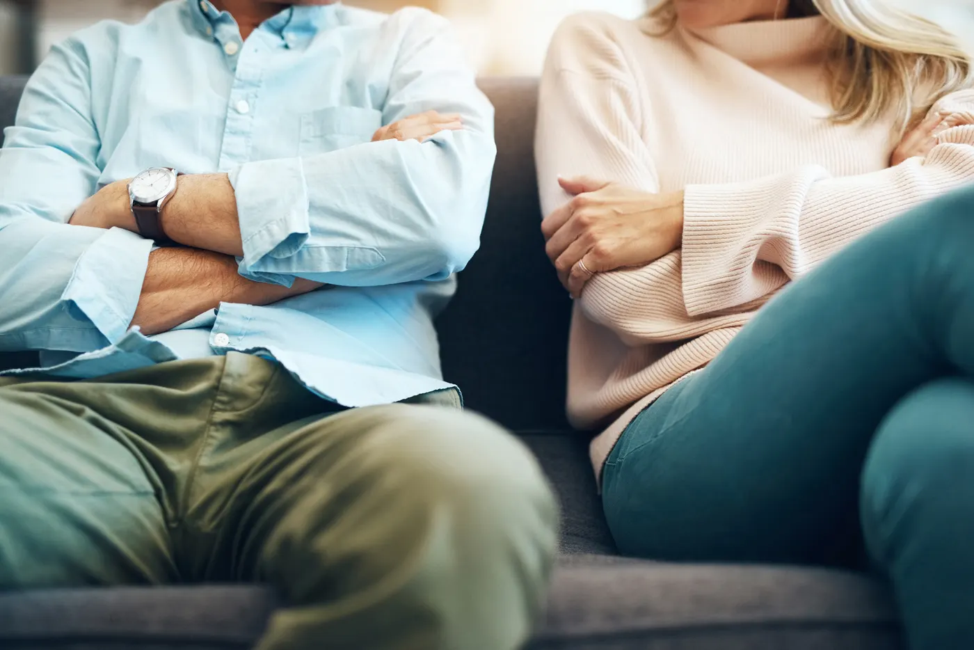 Ein Paar sitzt mit verschränkten Armen nebeneinander auf dem Sofa
